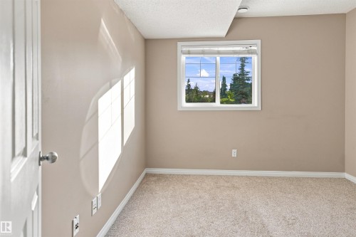Neutral-toned room featuring a white-framed window, textured carpeting, and a white paneled door - 1328 80 Street Sw, Edmonton, AB - Indoor Photo Showing Other Room