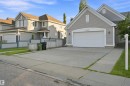 Front exterior featuring a light gray siding, an attached garage with an arched trim, a concrete driveway, a partial privacy fence, and mature landscaping - 1328 80 Street Sw, Edmonton, AB  - Outdoor With Facade 