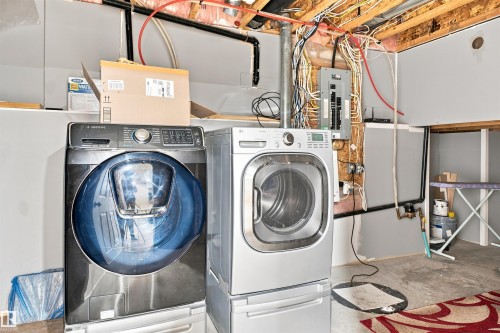 Dedicated laundry area featuring a front-load washer and dryer, exposed ceiling joists, and visible utility lines - 1328 80 Street Sw, Edmonton, AB - Indoor Photo Showing Laundry Room