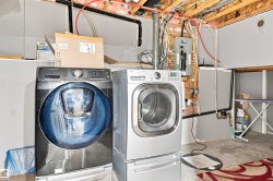 Dedicated laundry area featuring a front-load washer and dryer, exposed ceiling joists, and visible utility lines - 