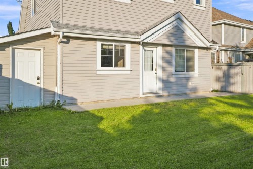 Rear exterior featuring light grey siding, a white entry door with a transom, a white four-panel door, and a grass area - 1328 80 Street Sw, Edmonton, AB - Outdoor