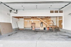 Spacious garage interior featuring concrete flooring, a white overhead garage door mechanism, an interior doorway, and unfinished framing with an exposed staircase - 