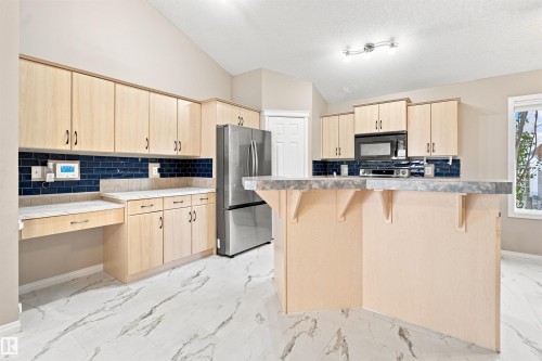 Kitchen featuring light wood-finish cabinetry, a blue subway tile backsplash, stainless steel appliances, and a central island with a breakfast bar - 1328 80 Street Sw, Edmonton, AB - Indoor Photo Showing Kitchen