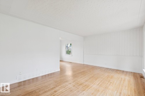 Spacious room featuring wood-finish flooring, white walls, and a textured ceiling - 8202 93A Avenue Nw, Edmonton, AB - Indoor Photo Showing Other Room