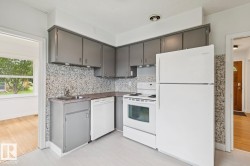 Kitchen featuring gray cabinetry, white appliances, a stone-finish backsplash, and light-toned flooring - 