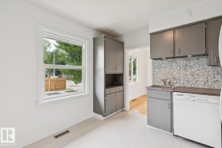 Kitchen featuring light wood-finish flooring, gray cabinetry, a gray mosaic tile backsplash, white appliances, and a double-pane window - 