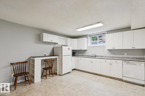 Kitchen featuring white cabinetry, a white refrigerator, a white dishwasher, a built-in sink, and light-toned flooring - 8202 93A Avenue Nw, Edmonton, AB - Indoor Photo Showing Kitchen With Double Sink