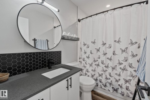 Bathroom featuring a dark gray countertop, black hexagonal tile backsplash, white vanity cabinetry with black hardware, and an undermount sink with a matte black faucet - 4723 105 Street Nw, Edmonton, AB - Indoor Photo Showing Bathroom