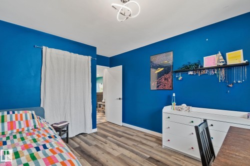 Spacious room featuring wood-finish flooring, a contemporary ceiling light fixture, vibrant blue walls, and white baseboards - 4723 105 Street Nw, Edmonton, AB - Indoor Photo Showing Bedroom