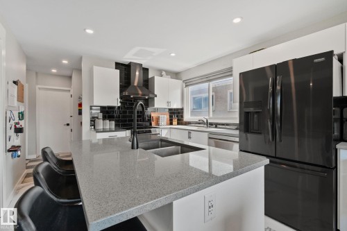 Kitchen featuring a large island with an undermount sink, light-toned countertop, and matte black faucet - 4723 105 Street Nw, Edmonton, AB - Indoor Photo Showing Kitchen With Double Sink With Upgraded Kitchen