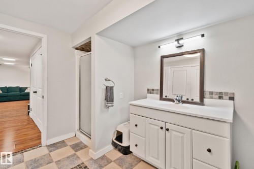 Bathroom featuring a white vanity with panel cabinetry and a white countertop, a framed mirror, and a linear vanity light fixture - 4723 105 Street Nw, Edmonton, AB - Indoor Photo Showing Bathroom