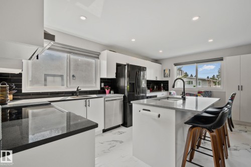 Modern kitchen featuring an island with seating, dark countertops, white cabinetry, a black tile backsplash, and stainless steel appliances - 4723 105 Street Nw, Edmonton, AB - Indoor Photo Showing Kitchen