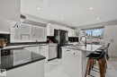 Modern kitchen featuring an island with seating, dark countertops, white cabinetry, a black tile backsplash, and stainless steel appliances - 4723 105 Street Nw, Edmonton, AB  - Indoor Photo Showing Kitchen 