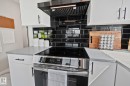 Contemporary kitchen featuring sleek black subway tile backsplash, white cabinetry with matte black hardware, light-toned countertops, and a built-in stainless steel range with a black hood - 4723 105 Street Nw, Edmonton, AB  - Indoor Photo Showing Kitchen 