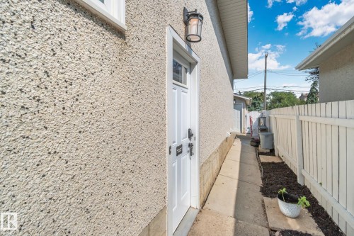Exterior wall with stucco finish, featuring a white pedestrian door with hardware, and an exterior wall lantern - 4723 105 Street Nw, Edmonton, AB - Outdoor
