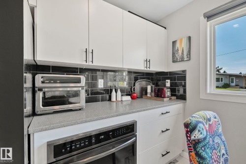 White upper and lower cabinetry with matte black hardware, black subway tile backsplash, light grey countertop, and a built-in stainless steel oven - 4723 105 Street Nw, Edmonton, AB - Indoor Photo Showing Kitchen