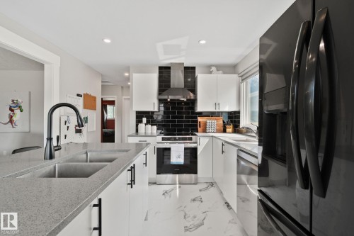 Modern kitchen featuring white cabinetry, black subway tile backsplash, stainless steel appliances, and sleek stone-finish countertops with an undermount double sink - 4723 105 Street Nw, Edmonton, AB - Indoor Photo Showing Kitchen With Double Sink With Upgraded Kitchen