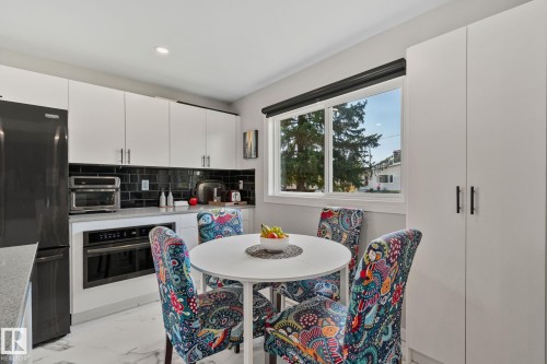 Modern kitchen featuring white cabinetry, black subway tile backsplash, light-toned countertops, and integrated black appliances - 4723 105 Street Nw, Edmonton, AB - Indoor