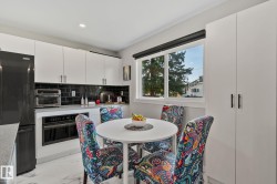 Modern kitchen featuring white cabinetry, black subway tile backsplash, light-toned countertops, and integrated black appliances - 