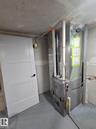 Modern HVAC system with exposed ductwork, concrete flooring, and a white three-panel door - 228 36 Street Sw, Edmonton, AB - Indoor Photo Showing Other Room