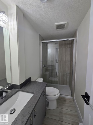 Full bathroom with a walk-in shower featuring a glass enclosure and wood-finish tile surround - 228 36 Street Sw, Edmonton, AB - Indoor Photo Showing Bathroom