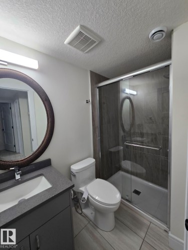 Modern bathroom featuring a sleek vanity with integrated sink and ample counter space, a contemporary toilet, and a walk-in shower enclosure with dark tile surround - 228 36 Street Sw, Edmonton, AB - Indoor Photo Showing Bathroom