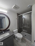 Modern bathroom featuring a sleek vanity with integrated sink and ample counter space, a contemporary toilet, and a walk-in shower enclosure with dark tile surround - 