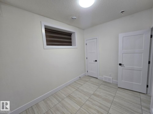 Room featuring tiled flooring, a window with roller blinds, and two paneled doors with black hardware - 228 36 Street Sw, Edmonton, AB - Indoor Photo Showing Other Room