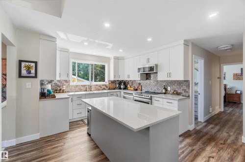 Contemporary kitchen featuring a central island with a solid surface countertop, white cabinetry with modern hardware, stainless steel appliances, a mosaic tile backsplash, and wood-finish flooring - 11351 35A Avenue Nw, Edmonton, AB - Indoor Photo Showing Kitchen With Upgraded Kitchen