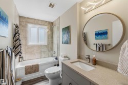 Bathroom featuring a vanity with an integrated sink, a large round mirror, modern overhead lighting, a tub with a tile surround, and wood-finish flooring - 