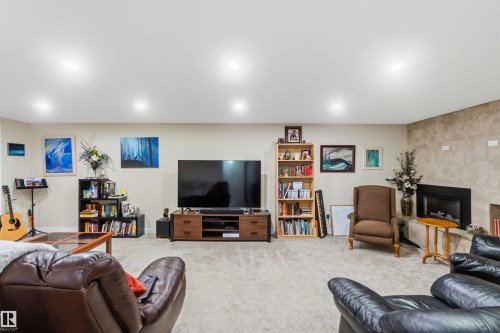 Spacious entertainment room featuring recessed lighting, light-toned carpeting, a built-in fireplace with a stone-finish surround, and neutral wall tones - 11351 35A Avenue Nw, Edmonton, AB - Indoor Photo Showing Basement
