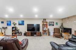 Spacious entertainment room featuring recessed lighting, light-toned carpeting, a built-in fireplace with a stone-finish surround, and neutral wall tones - 