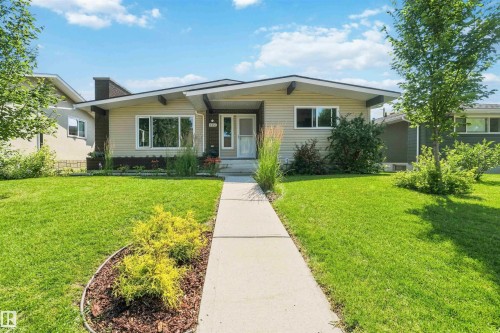 Mid-century modern facade with beige siding, a dark trim roofline, large windows, an integrated planter box, and a concrete pathway - 11351 35A Avenue Nw, Edmonton, AB - Outdoor With Facade