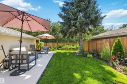 Expansive backyard featuring a concrete patio, lush green lawn, mature trees, and a wooden privacy fence - 