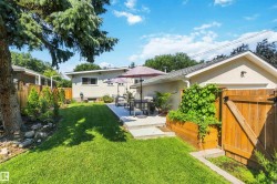 Spacious backyard featuring a manicured lawn, a concrete patio, a wooden privacy fence, a raised garden bed, and mature trees - 