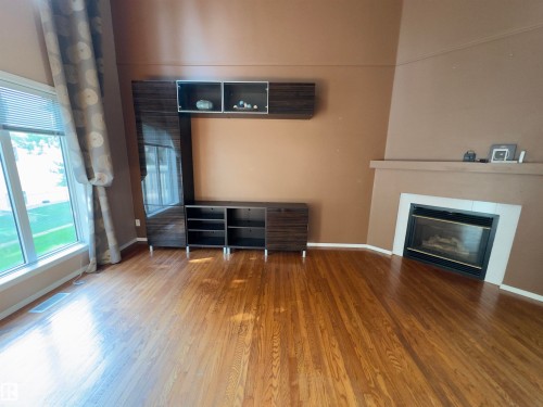 Hardwood flooring throughout featuring a corner fireplace with a white surround and a large window - #48 6608 158 Av Nw, Edmonton, AB - Indoor With Fireplace