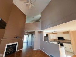 Vaulted ceilings featuring a ceiling fan, a fireplace with a white surround, wood-finish flooring, and a kitchen with white cabinetry and a built-in microwave - 