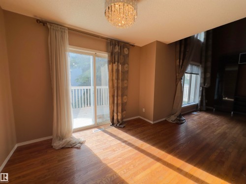 Spacious room featuring wood-finish flooring, a contemporary crystal chandelier, and a sliding glass door providing access to an exterior deck with white railings - #48 6608 158 Av Nw, Edmonton, AB - Indoor Photo Showing Other Room