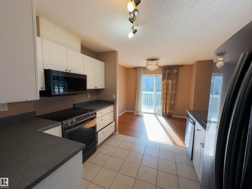 Kitchen featuring white cabinetry, dark speckled countertops, and an integrated black range with an overhead microwave - #48 6608 158 Av Nw, Edmonton, AB - Indoor Photo Showing Kitchen