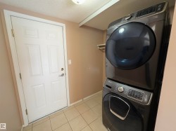 Laundry area featuring light-toned tile flooring, light neutral wall paint, and a stacked washer and dryer unit - 