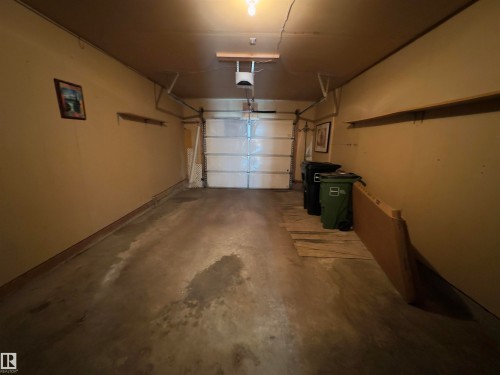 Single-car garage featuring a sectional overhead door, painted walls, concrete flooring, and an overhead light fixture - #48 6608 158 Av Nw, Edmonton, AB - Indoor Photo Showing Garage