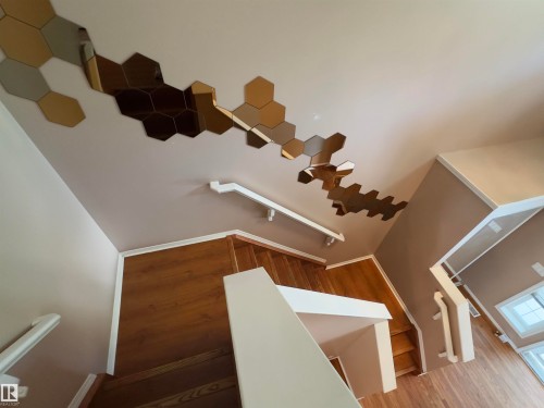 Stairwell featuring wood-finish treads and risers, white handrails, and a contemporary hexagonal mirror wall installation - #48 6608 158 Av Nw, Edmonton, AB - Indoor Photo Showing Other Room