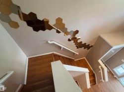Stairwell featuring wood-finish treads and risers, white handrails, and a contemporary hexagonal mirror wall installation - 