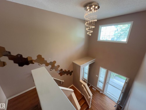 Two-story entryway featuring wood-finish flooring, a contemporary chandelier with crystal accents, and multiple windows providing natural illumination - #48 6608 158 Av Nw, Edmonton, AB - Indoor Photo Showing Other Room