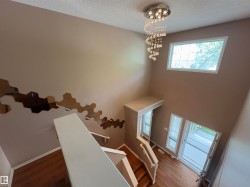 Two-story entryway featuring wood-finish flooring, a contemporary chandelier with crystal accents, and multiple windows providing natural illumination - 