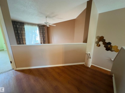 Split-level floor plan featuring wood-finish flooring, a contemporary ceiling fan, and a half-wall partition - #48 6608 158 Av Nw, Edmonton, AB - Indoor Photo Showing Other Room
