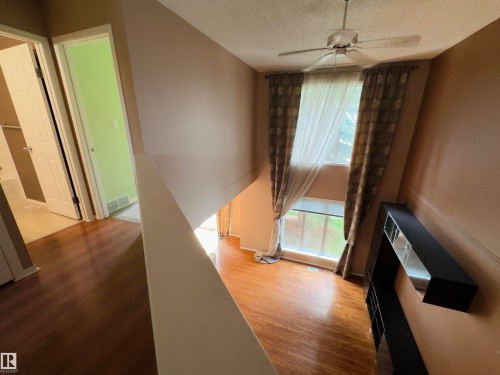 Upper-level hallway with wood-finish flooring, white doors, and a partial railing overlooking a double-height space - #48 6608 158 Av Nw, Edmonton, AB - Indoor Photo Showing Other Room