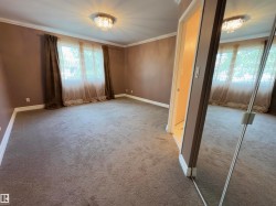 Spacious room featuring neutral carpeting, a large window with drapes, crown molding, and a crystal flush-mount light fixture - 