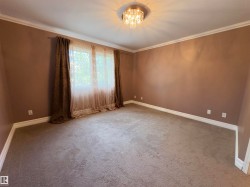 Spacious room featuring neutral carpeting, crown molding, and a chandelier light fixture - 