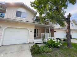 Exterior featuring light-toned horizontal siding, a single-car garage, covered entry porch, established front landscaping, and a prominent mature tree - 
